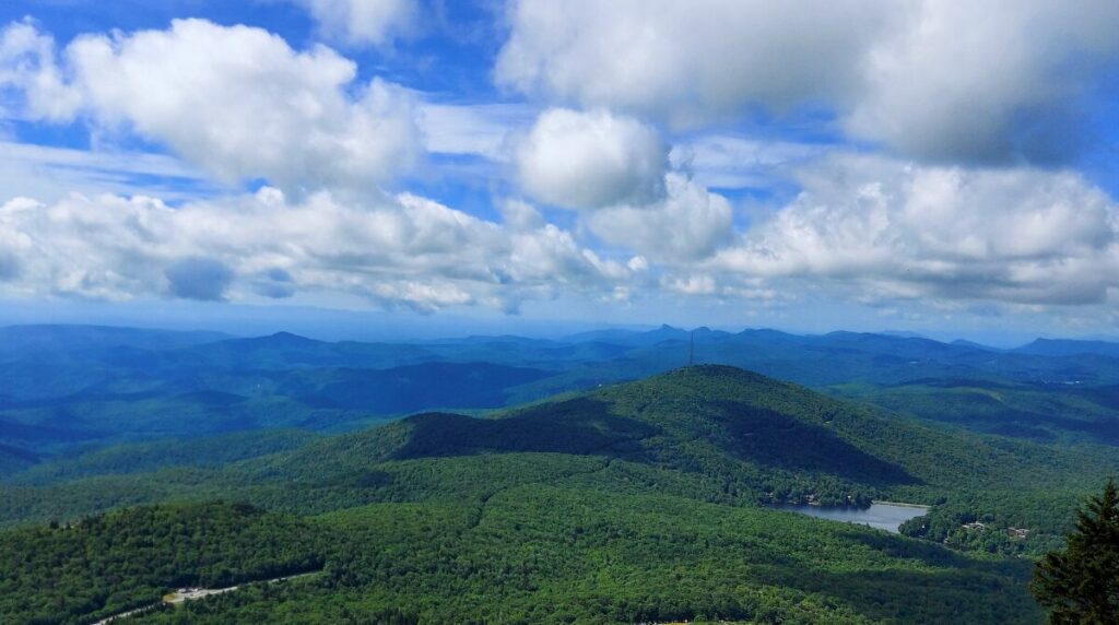 The view from Linville Peak at Grandfather Mountain State park rolling and jagged green hills with cotton candy clouds